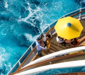 Eine Freundesgruppe an Bord der Costa Diadema. Das Foto ist von oben aufgenommen, sodass das wellige Meer und der gespannte Sonnenschirm sichtbar sind.