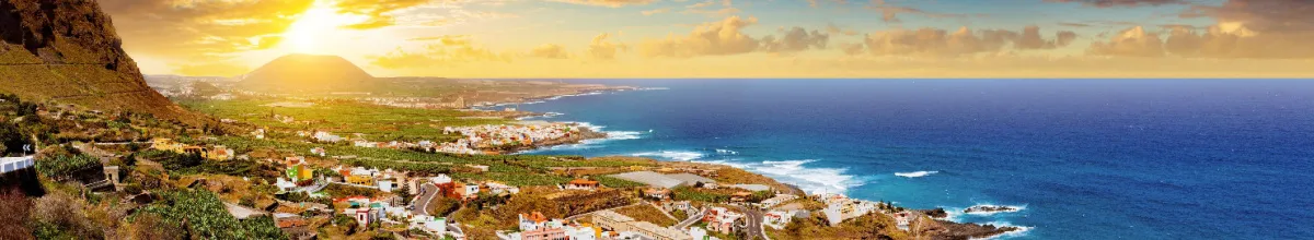 Sonnenuntergang über dem Atlantik auf Teneriffa Panoramablick über die grüne Küste einer Kanarischen Insel mit Bananenplantagen und Meer bei Sonnenuntergang.