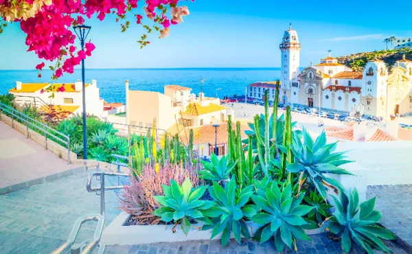 Landausflug Teneriffa: Basilika von Candelaria Blick auf die weiße Basilika von Candelaria auf Teneriffa mit dem blauen Atlantik und Blumen im Vordergrund.