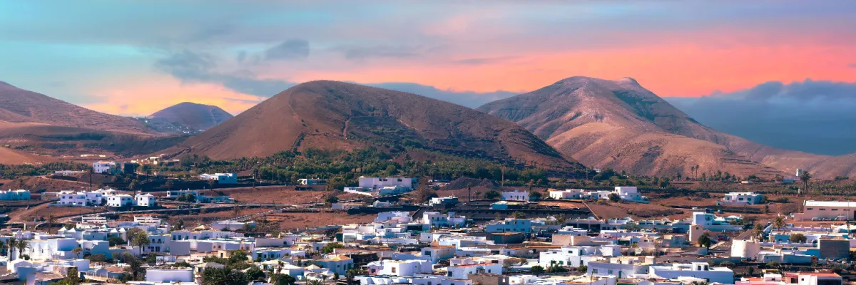Landausflug Lanzarote: Weiße Dörfer im Vulkanland Blick auf die typischen weißen Häuser von Lanzarote vor der Kulisse roter Vulkankegel im Abendlicht.