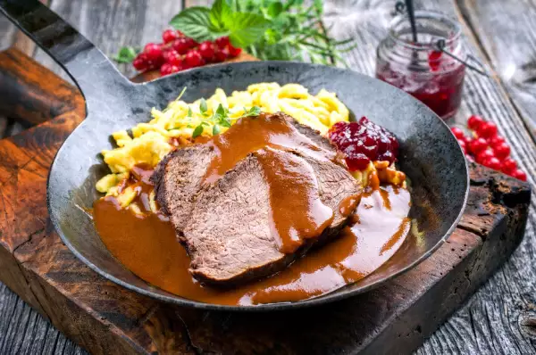 In einer gusseisernen Pfanne sind Sauerbraten mit Spätzle und Soße angerichtet.