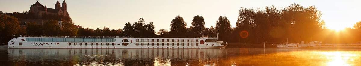 Kreuzfahrtschiff der A-ROSA fährt bei Sonnenuntergang über den Rhein.