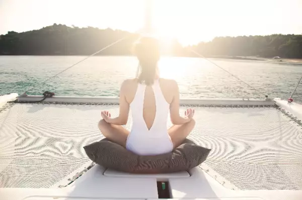 Eine Frau sitzt an Deck eines Kreuzfahrtschiffes und meditiert, während die Morgensonne erstahlt.