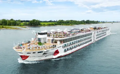 Draufsicht auf das moderne A-ROSA SENA Flussschiff mit dem Kussmund am Bug, das auf einem Fluss fährt. Das weitläufige Sonnendeck mit Pools, Liegen und Sonnenschirmen ist sichtbar.