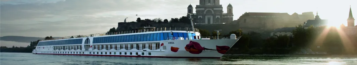 Ein A-ROSA Schiff mit dem charakteristischen Kussmund am Bug liegt auf einem Fluss, im Hintergrund die imposante Basilika von Esztergom in Ungarn bei Sonnenlicht.