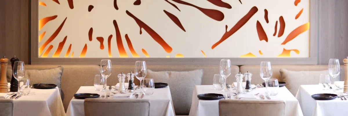 Ein stilvoll gedeckter Restaurantbereich an Bord eines A-ROSA Schiffes mit weißen Tischdecken, Gläsern, Besteck und schwarzen Tellern, im Hintergrund eine moderne Wanddekoration in Orange- und Beigetönen.