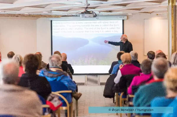 Am Board steht ein älterer Mann der den Passagieren etwas erklärt und beibringt.