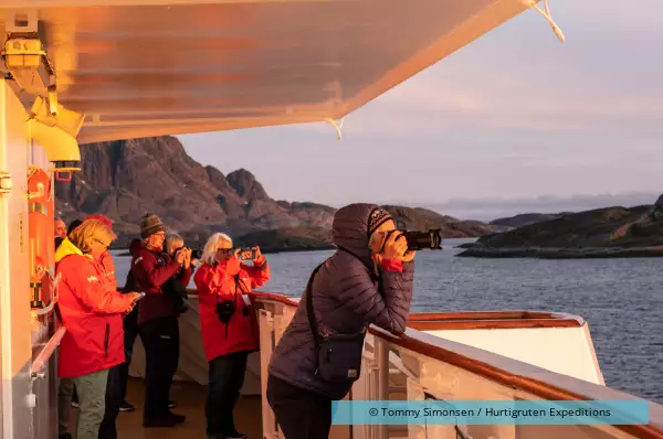 An Bord der MS Nordkapp schaut eine Gruppe Kreuzfahrtgäste von Hurtigruten der Sonne entgegen.