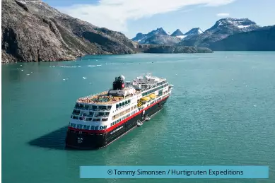 Vor den pompösen Bergen fährt ein Kreuzfahrtschiff.