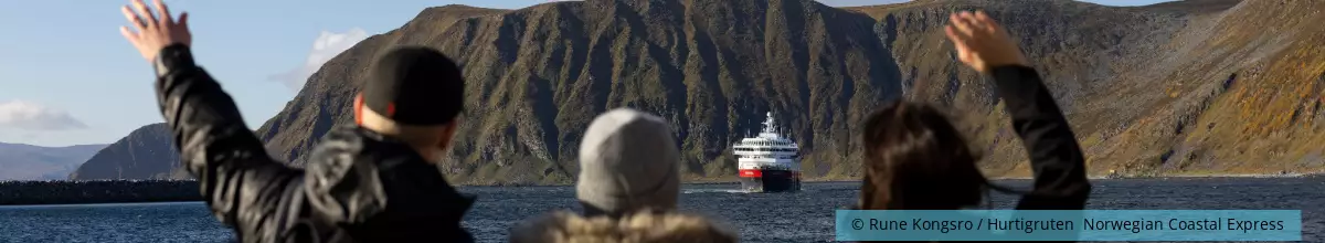 Drei Passagiere winken dem Kreuzfahrtschiff zu.