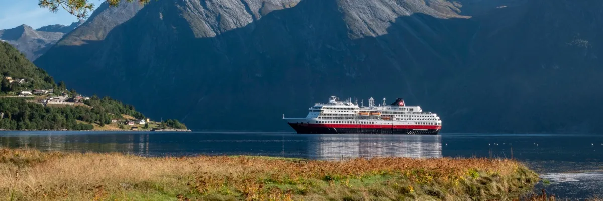 Ein Schiff von Hurtigruten im Fjord vor dem kleinen Dorf Sæbø im Hjørundfjord, Norwegen.