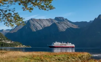 Die Reederei Hurtigruten Ein Schiff der Reederei Hurtigruten schwimmt durch einen Fjord in Norwegen an einem herbstlichen Tag.
