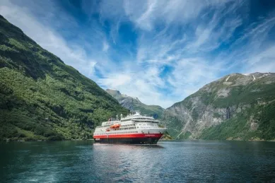 Die MS Finnmarken fährt durch einen Fjord in Norwegen mit einem grünen Bergpanorama im Hintergrund.