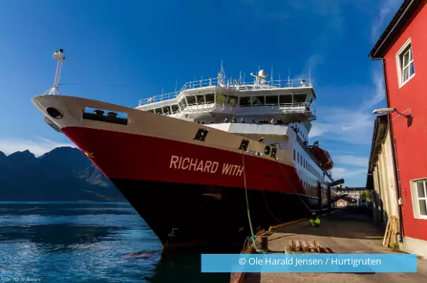 Die MS Richard With legt an einem kleinen norwegischen Hafen mit roten Häusern an, um die Post abzuliefern.