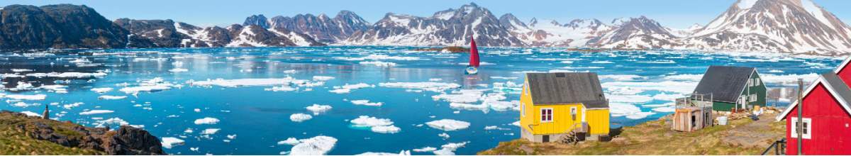 Eine Yacht mit roten Segel in Bewegung - Panoramasicht auf das bunte Kulusuk-Dorf in Ostgrönland