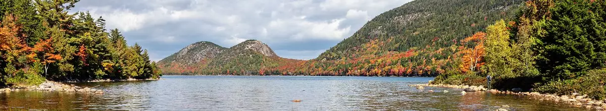 Einblick in den wunderschönen Arcadia Nationalpark, den Sie während Ihrer Expeditions-Seereise nach Nordamerika besichtigen können. Die Blätter der Bäume verfärben sich langsam orange und im Vordergrund befindet sich ein See.