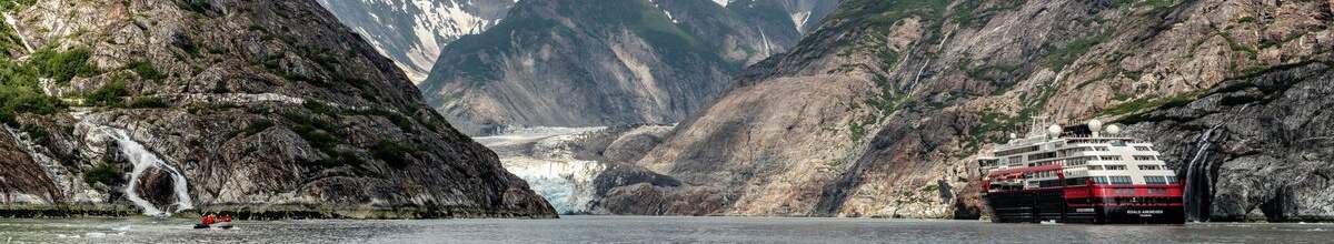 Ein Expeditionsschiff ist rechts im Bild. Im Rest des Bildes sieht man das Gebirge von Alaska.