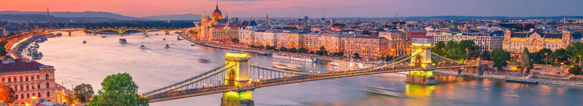 Die Stadt Budapest liegt an der Donau. Die Stadt ist erleuchtet und die Sonne geht farbenfroh unter.