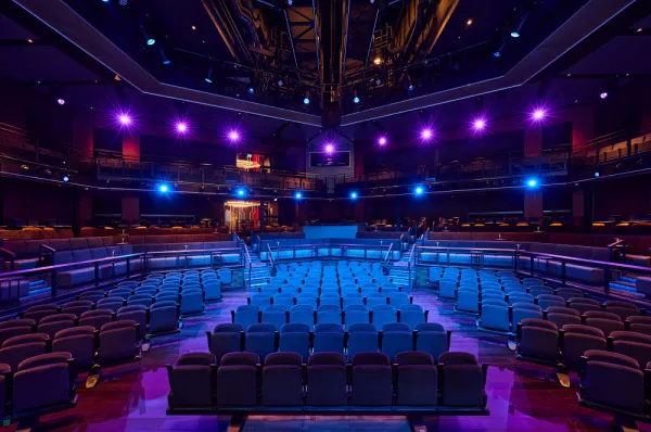 Blick von der Bühne in das leere, modern gestaltete Haupttheater der <i>Mein Schiff Relax</i>, das mit blauen und violetten Lichtern stimmungsvoll beleuchtet ist.