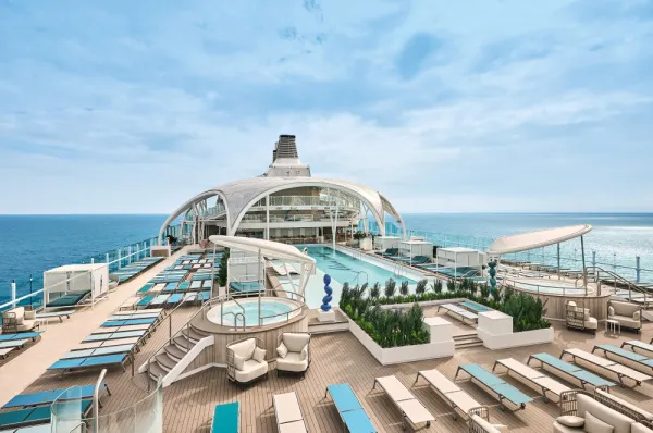 Weitwinkelaufnahme des Hauptpooldecks der <i>Mein Schiff Relax</i> mit dem großen 25-Meter-Außenpool und zwei Whirlpools, überdacht vom markanten Marcoon-Dach. Zahlreiche Sonnenliegen stehen bereit, während das Schiff auf dem offenen Meer fährt.