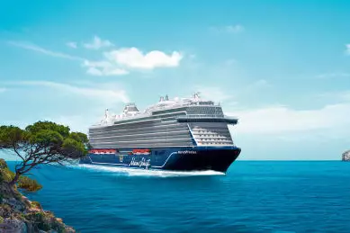 Frontalansicht des neuen Kreuzfahrtschiffes <i>Mein Schiff Relax</i> von TUI Cruises, das bei sonnigem Wetter auf dem blauen Meer entlang einer mediterranen Felsküste fährt.