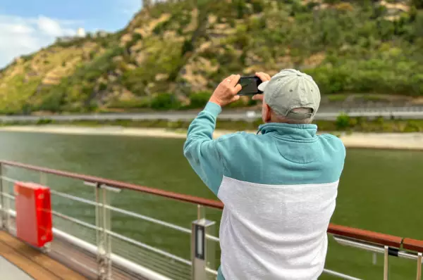 Mann steht auf Sonnendeck eines Schiffes und nimmt ein Foto auf.