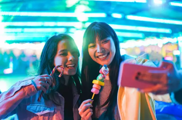 Spaß im Freizeitpark Zwei Frauen machen ein Selfie und essen Süßigkeiten.