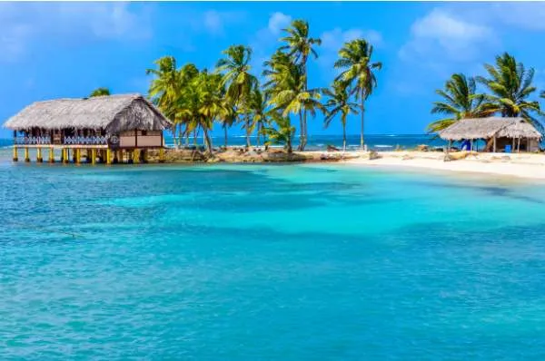 Authentische Kultur als Grund für eine Karibik-Kreuzfahrt Eine kleine, tropische Insel mit Palmen und Holzhütten als Grund für eine Karibik-Kreuzfahrt. Eine Hütte mit Strohdach steht auf Stelzen im türkisfarbenen Wasser und symbolisiert die Entdeckung von authentischen Orten und der lokalen Kultur.