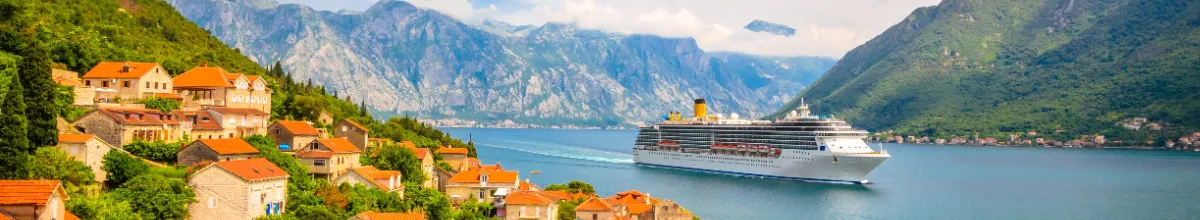 Panorama eines Kreuzfahrtschiffes in einer malerischen Mittelmeerbucht mit historischen Häusern am Ufer und Bergen im Hintergrund, das zur Buchung einer Mittelmeerkreuzfahrt einlädt.