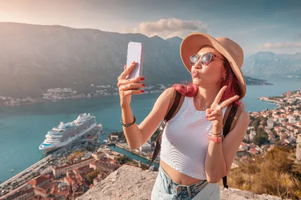 Junge Frau posiert für einen Selfie auf einem Aussichtspunkt am Meer, Symbol für die vielfältigen Reiseerlebnisse, die eine Mittelmeerkreuzfahrt für jeden Reisetyp bietet.