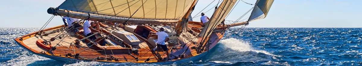 Segelyacht bei starkem Wellengang auf blauem Meer unter sonnigem Himmel, Symbol für eine dynamische Kreuzfahrt und die Herausforderung der Seekrankheit.