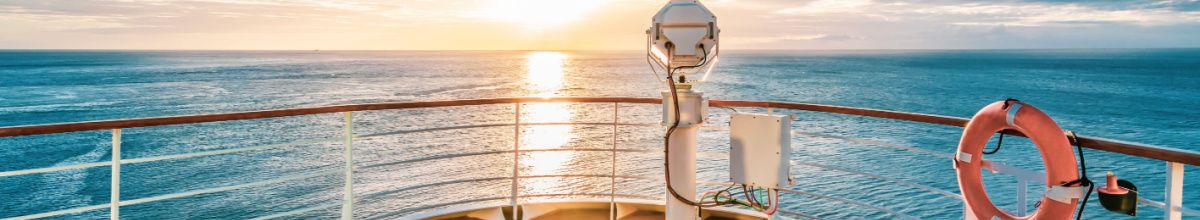 Ein Deck eines Kreuzfahrtschiffes bei Sonnenaufgang mit einem Rettungsrings an der Reling rechts.