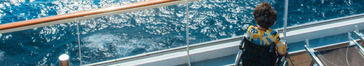 Frau in Rollstuhl sitzt an Deck und blickt aufs Meer.