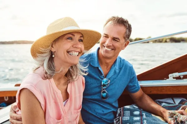 Ein Pärchen sitze in Casual, also Freizeitbekleidung, auf einem Schiff. Dazu gehört ein Polohemd, Hut und Sonnenbrille.
