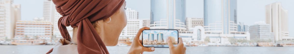 Eine Frau mit Kopftuch nimmt mit ihrem Handy ein Foto einer Skyline auf.