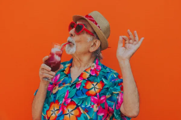 Ein stilvoller Senior mit Hut und Sonnenbrille trinkt genüsslich einen bunten Cocktail. Das Bild steht für die Lebensfreude und die entspannte Atmosphäre, die man auf einer unterhaltsamen Seniorenkreuzfahrt erlebt.
