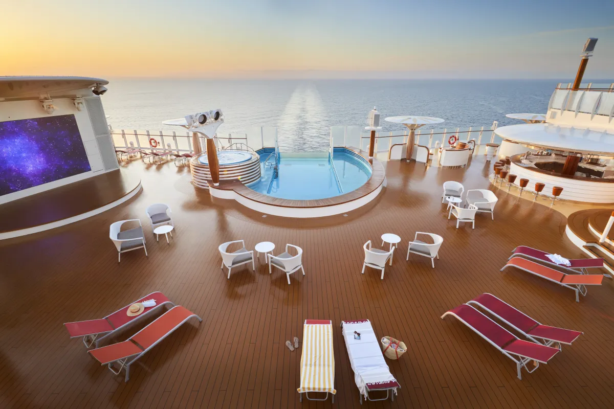 Das weite, sonnendurchflutete Ocean Deck auf AIDacosma mit Infinity-Pool, Whirlpool, stilvollen Sonnenliegen und Blick auf die Heckwelle im warmen Abendlicht.