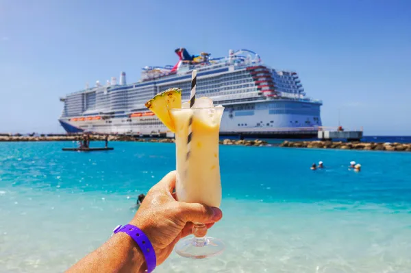Karibischer Cocktail-Genuss vor Anker liegendem Kreuzfahrtschiff Genussmoment: Cocktail in der Hand am tropischen Strand, großes Kreuzfahrtschiff im Hintergrund - typisch für Adults-Only Kreuzfahrt-Urlaub.
