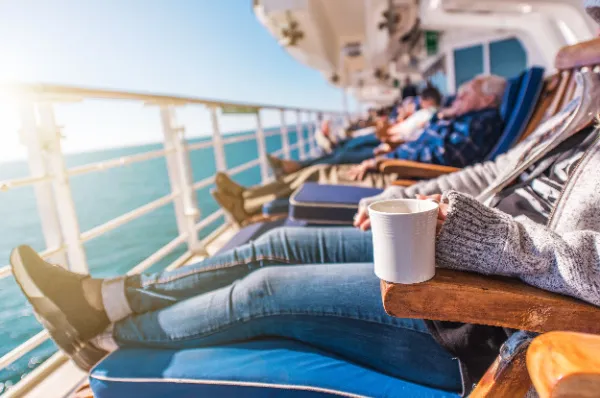 Gemütliche Auszeit an Deck mit Meerblick Entspannte Passagiere genießen die Sonne und den Meerblick in Liegestühlen auf dem Deck eines Kreuzfahrtschiffes, eine Person hält eine Tasse - Ruhe auf See bei einer Adults-Only Kreuzfahrt.