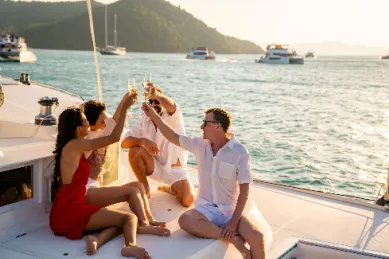 Gruppe von vier Erwachsenen stößt mit Champagnergläsern auf dem Deck einer Yacht bei Sonnenuntergang an – Symbol für Genuss auf einer Adults-Only Kreuzfahrt.