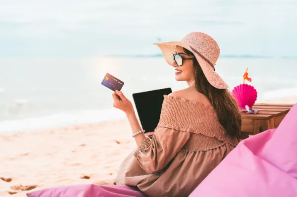 Vorfreude: Single Kreuzfahrt bequem online buchen Frau im Sommerkleid und Hut am Strand bucht am Laptop mit Kreditkarte ihre Reise - Symbolbild für die einfache Online-Buchung einer Single Kreuzfahrt.