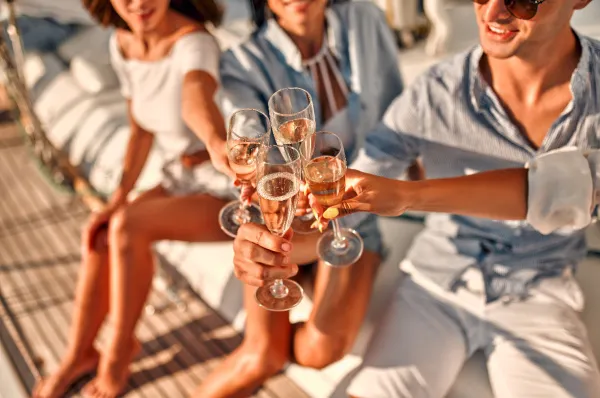 Anschluss finden auf der Single Kreuzfahrt: Gemeinsam anstoßen Gruppe junger Leute stößt bei Sonnenschein auf dem Holzdeck eines Schiffes mit Sektgläsern an – Symbol für Geselligkeit und neue Freundschaften auf Single Kreuzfahrten.