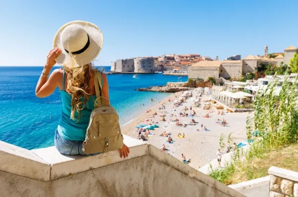 Strand in Dubrovnik Eine Touristin sitzt auf einer Mauer und blickt auf den Strand von Dubrovnik herunter.