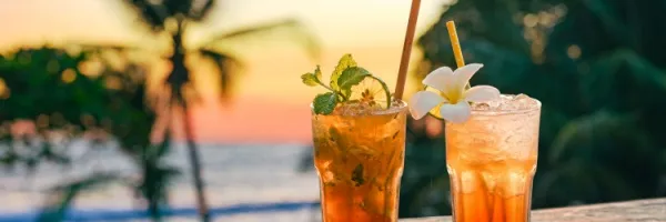 Zwei Cocktails mit Palmen im Hintergrund im Sonnenuntergang an einem Strand.