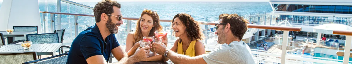 Eine Gruppe von Freunden stößt mit farbenfrohen Cocktails auf dem sonnigen Außendeck eines Schiffes von Norwegian Cruise Line an.