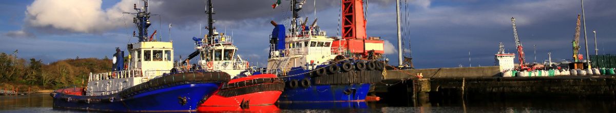 Drei Fischerboote im Hafen von Foynes in Irland mit einem Teil des Hafens im Hintergrund.