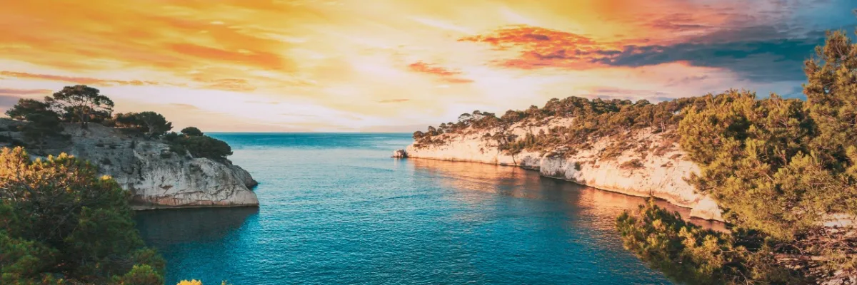 Weiße, baumbestandene Felsküste der Calanques im Sonnenaufgang.