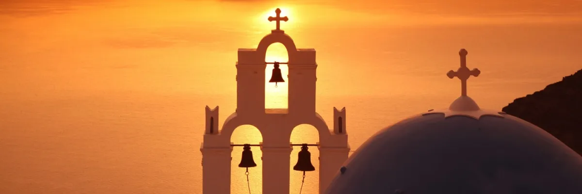 Glockenturm und blaue Kuppel einer Kirche von Santorini im Sonnenuntergang.