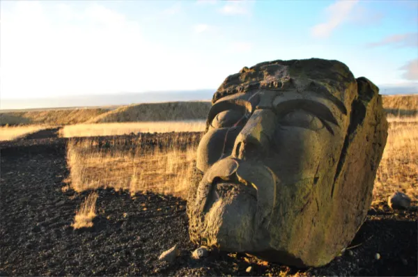 Der Kopf einer alten Steinskulptur auf einem Feld bei Sonnenschein.
