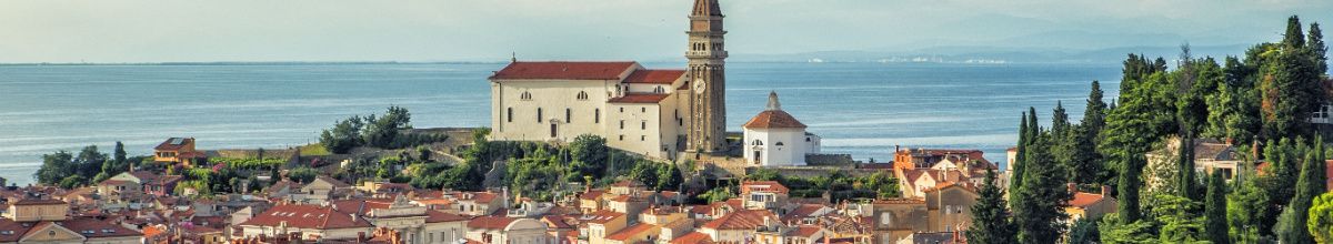 Eine Kirche auf einem Berg in Koper, die eine rustikal wirkende Stadt überblickt mit dem Meer im Hintergrund.